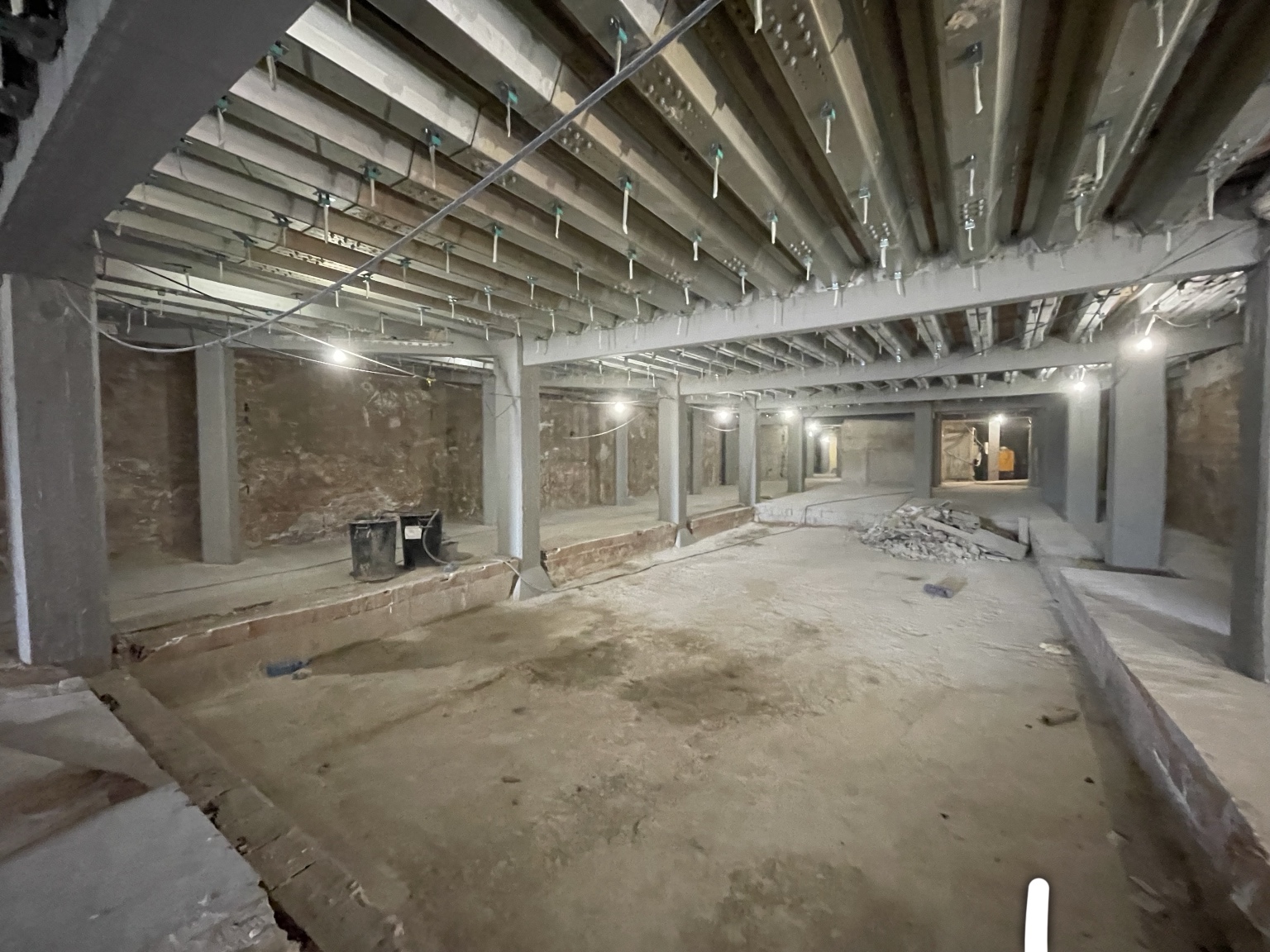 The DONDA club basement under construction: concrete columns supporting new steel reinforcement beams, exposed brick walls