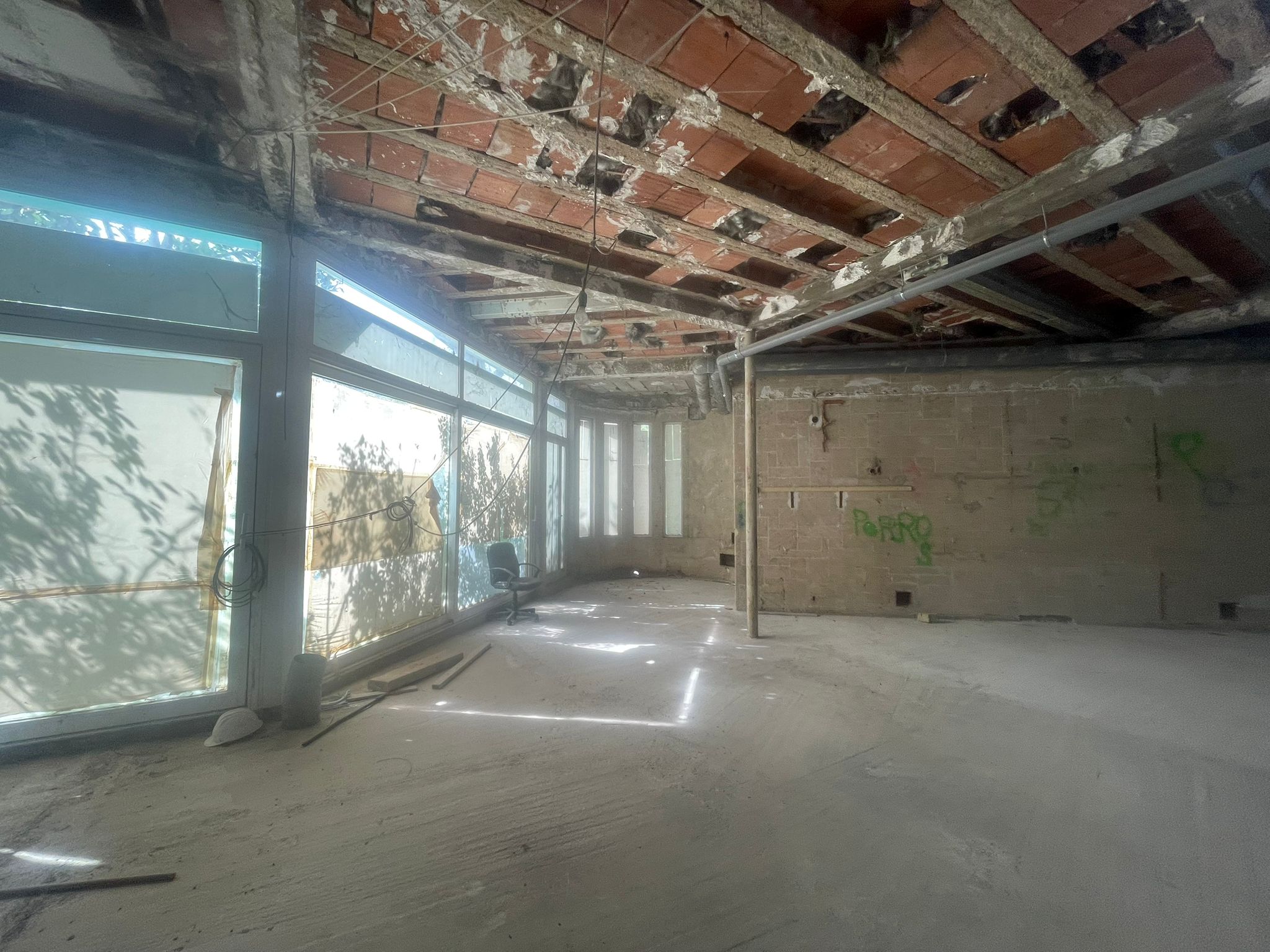 The future restaurant level mid-construction: exposed brick-and-iron ceiling joists, raw concrete floor, glass façade pulling daylight in from the Paseo